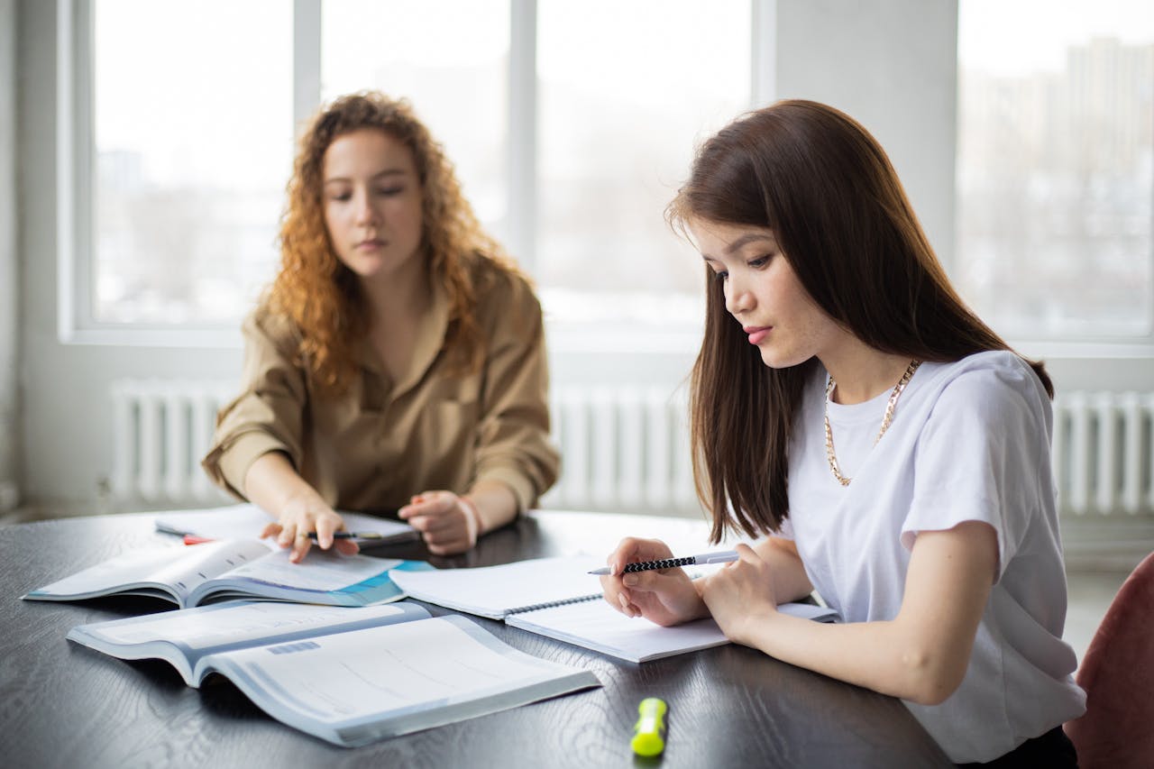why-choose-us Two young women concentrating on study materials in a well-lit classroom environment.