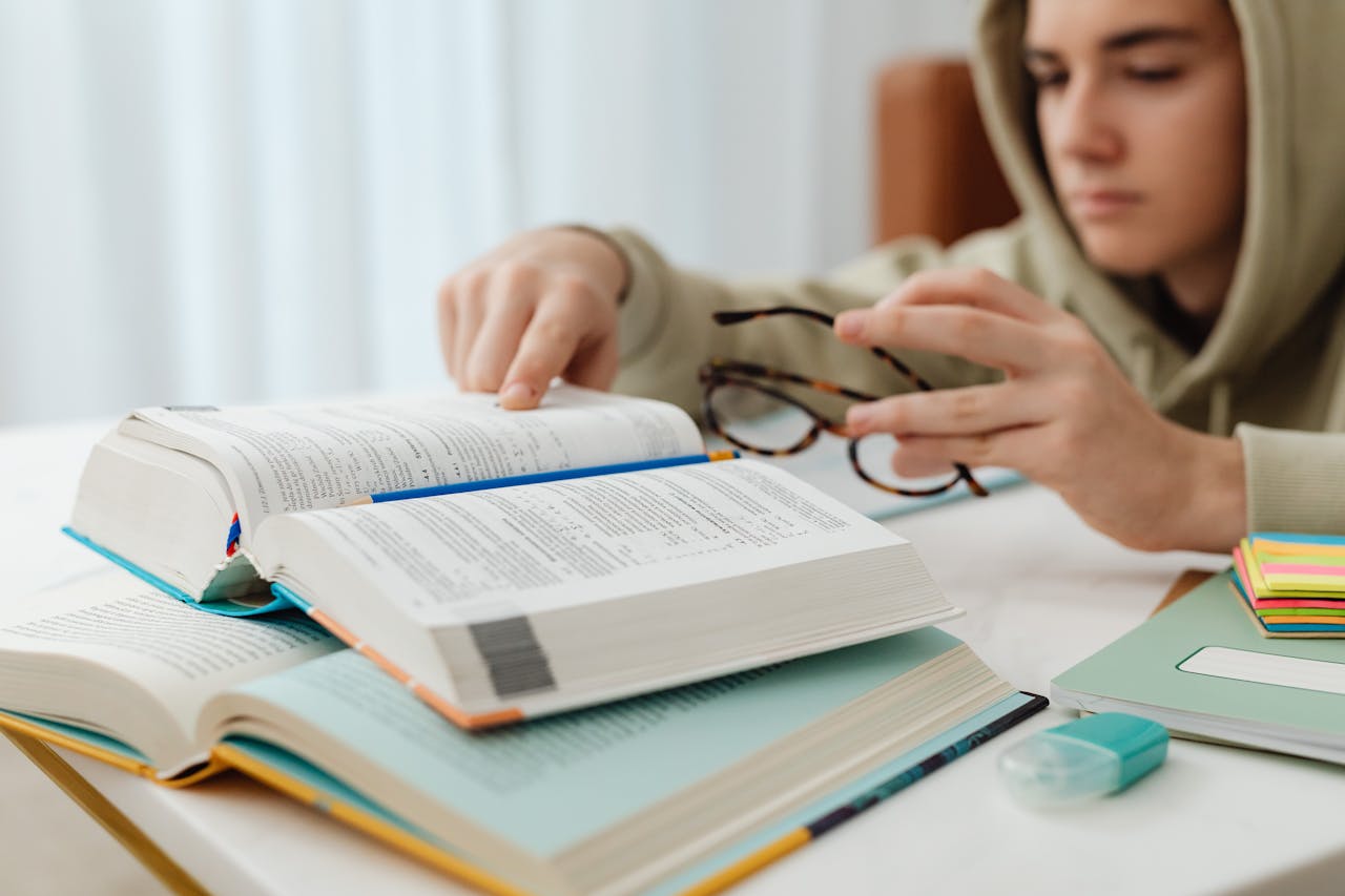 services-02 Focused teenager studying with open textbooks, eyeglasses, and notes.
