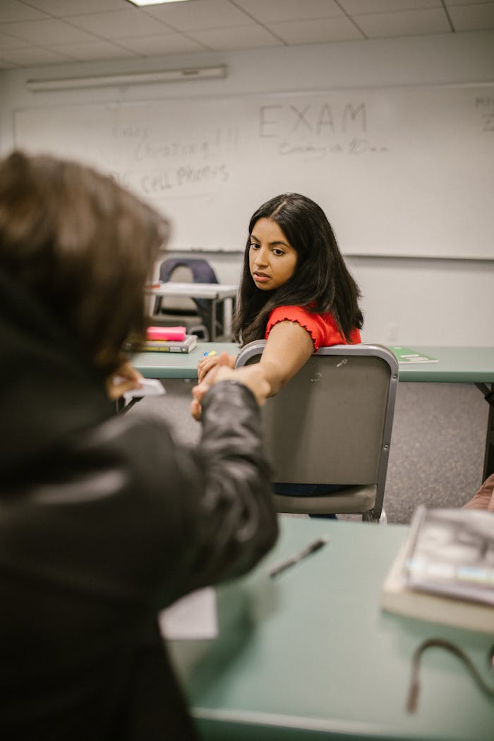 services-01 Two students subtly exchanging notes during an exam in a classroom setting.