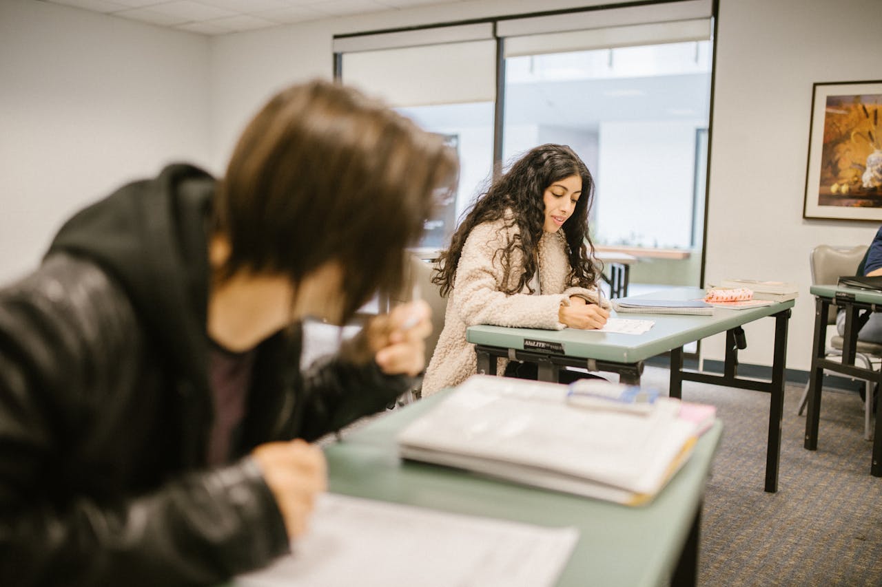 gallery-2 Two students focused on an exam in a classroom setting during daylight.