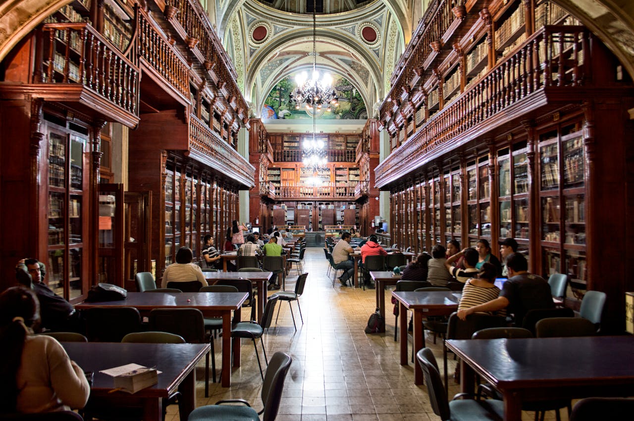 about-01 Elegant library with people studying, surrounded by wooden shelves and classical architecture.