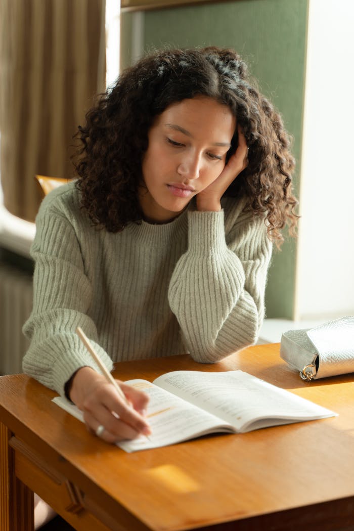 gallery-3 Teenage girl with curly hair studying at a desk, concentrated on her homework.